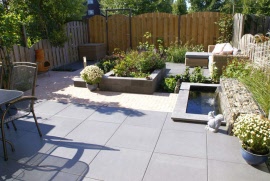 Strakke moderne tuin met schanskorf, waterelement en borderbak